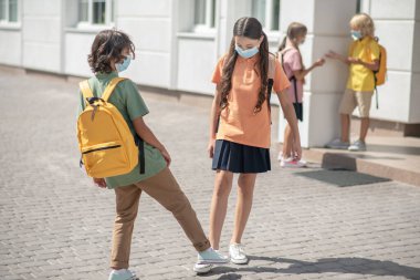 Okul bahçesindeki koruyucu maskeli çocuklar birbirlerine mesafeli davranıyorlar.