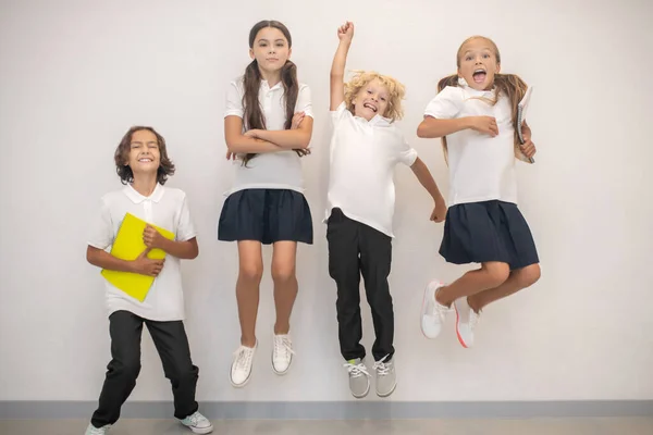 Uczniowie skaczą przy ścianie i wyglądają na zadowolonych. — Zdjęcie stockowe