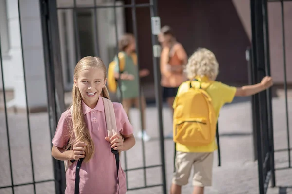 Roztomilé školačka s batohem s pozitivním úsměvem při čekání na svého přítele — Stock fotografie