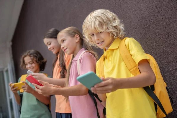 Quatre enfants debout les uns à côté des autres avec des smartphones dans les mains et jouer en ligne — Photo
