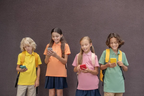 Cuatro niños jugando juegos en línea en sus teléfonos inteligentes — Foto de Stock