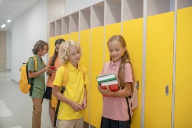 Kız ve erkek okul koridorunda dolapların yanında konuşuyorlar.