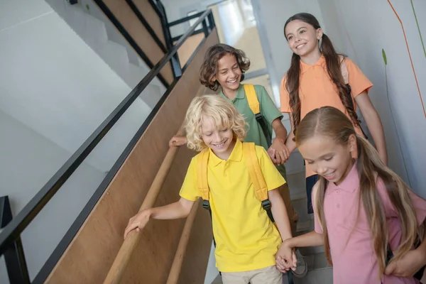 School friends going downstairs, holding hands and looking happy