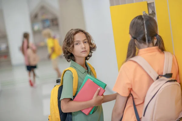 Dark-haired boy talking to his classmate in a school corridor