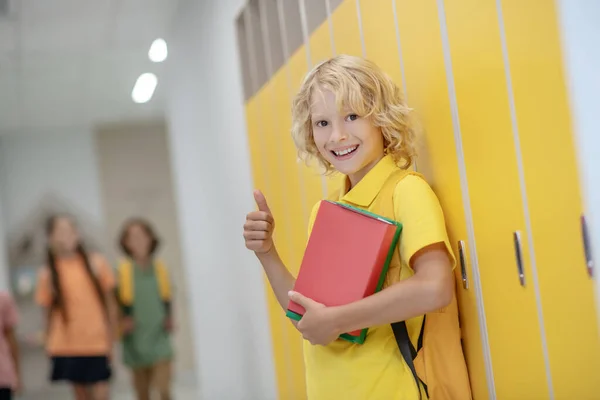 Blondýny s úsměvem chlapec ve žluté tričko stojící v blízkosti skříněk na chodbě — Stock fotografie