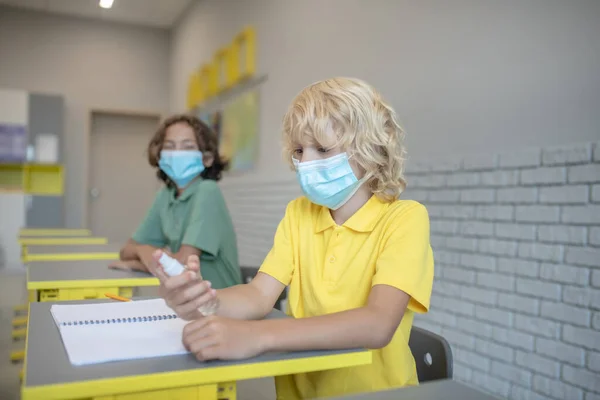 Fagert hår pojke i en mask sprutar sanitetsrengöringsmedel på händerna — Stockfoto