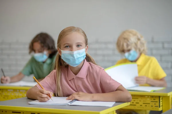 Flicka i mask sitter på lektionen och tittar koncentrerad — Stockfoto