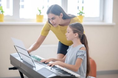 Kız ve öğretmeni müzik metnine bakıyorlar ve ilgili görünüyorlar.