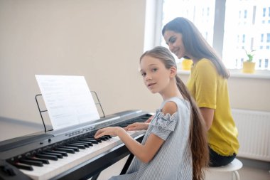 Kız ve öğretmeni birlikte piyano çalıyor ve kendilerini iyi hissediyorlar.