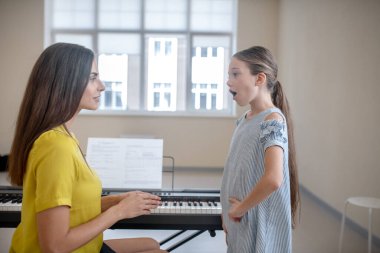 Girl in a blue dress having a vocal lesson clipart