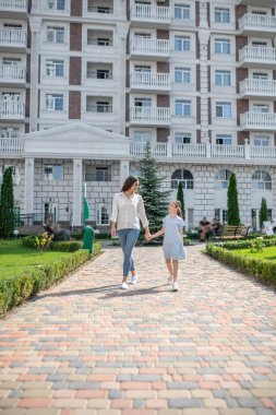 Anne ve kızı yürüyor ve el ele tutuşuyorlar.