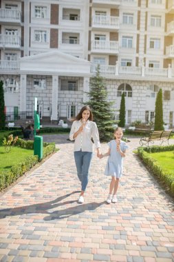 Anne ve kızı birlikte yürüyor ve dondurma yiyorlar.