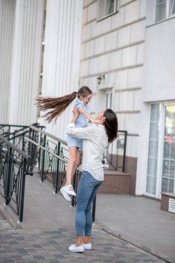 Koyu saçlı anne mutlu çocuğunu kucağında tutuyor ve gülümsüyor.