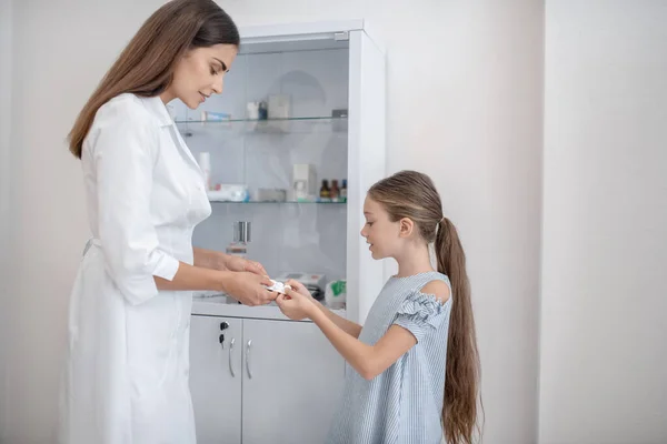 Mooie dokter in een labjas die pillen geeft aan een meisje. — Stockfoto