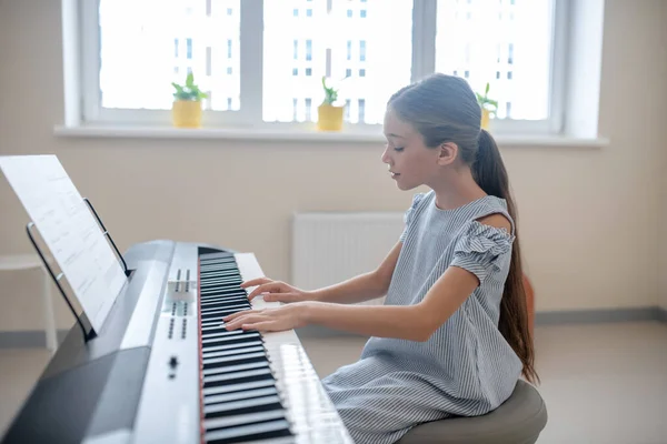 Lang haar meisje in blauwe jurk zittend aan de piano — Stockfoto