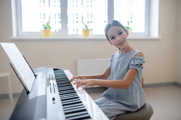 Lang haar meisje in blauwe jurk zitten aan de synthesizer en glimlachen — Stockfoto