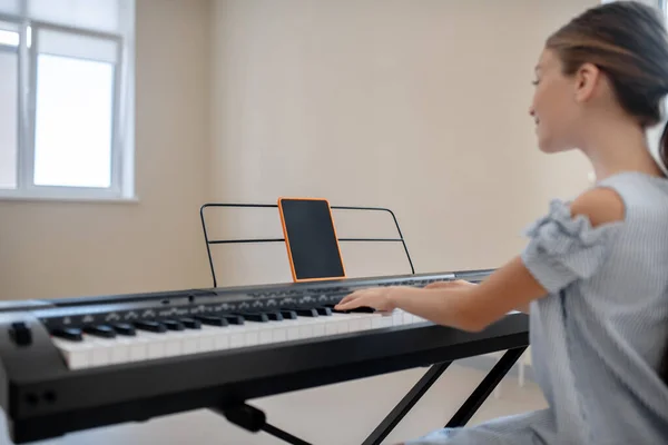 Lang haar meisje in blauwe jurk zitten aan de synthesizer en oefenen — Stockfoto