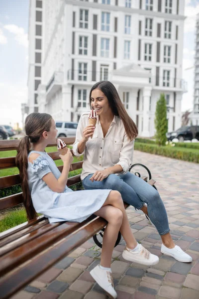 Η μαμά και η κόρη κάθονται στον πάγκο και απολαμβάνουν παγωτό. — Φωτογραφία Αρχείου
