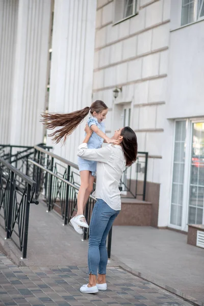 Koyu saçlı anne mutlu çocuğunu kucağında tutuyor ve gülümsüyor.