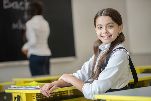 Colegiala sonriente sentada en el escritorio y sintiéndose bien —  Fotos de Stock