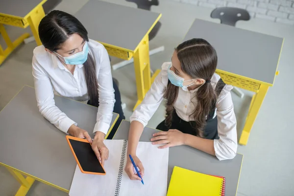 Lehrerin mit Schutzmaske im Gespräch mit ihrer Schülerin in einem Klassenzimmer — Stockfoto