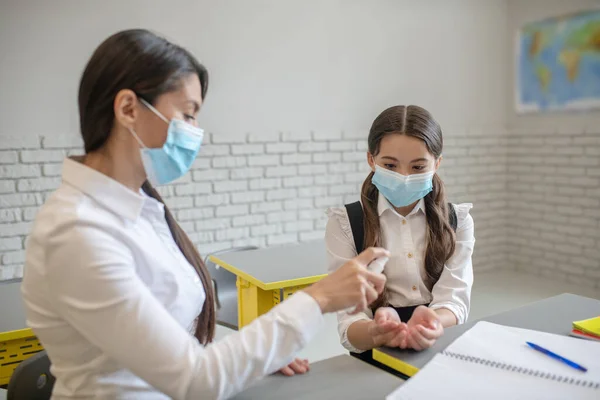 Lehrerin mit Schutzmaske desinfiziert die Hände ihrer Schüler — Stockfoto