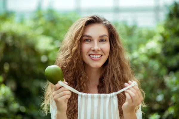 Mulher sorridente em camisa branca segurando abacate e sorrindo — Fotografia de Stock