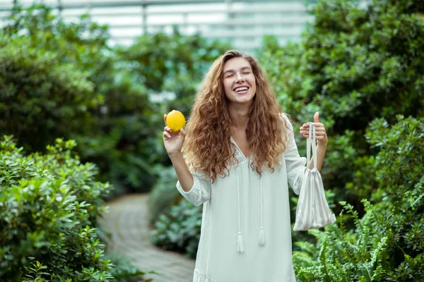 Kvinna i vit klänning håller en citron och ser glad ut — Stockfoto