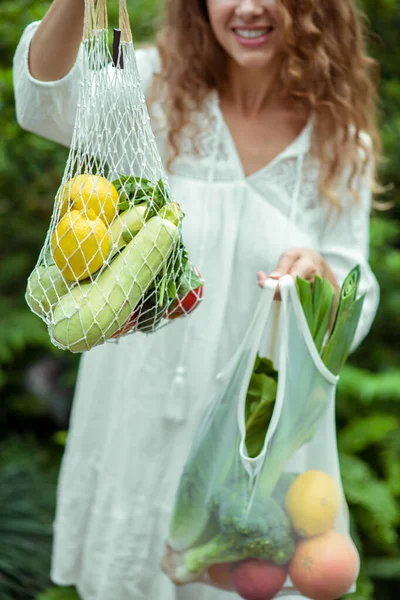 Vrouw in witte jurk draagtassen met verschillende groenten en een vrolijk gevoel — Stockfoto