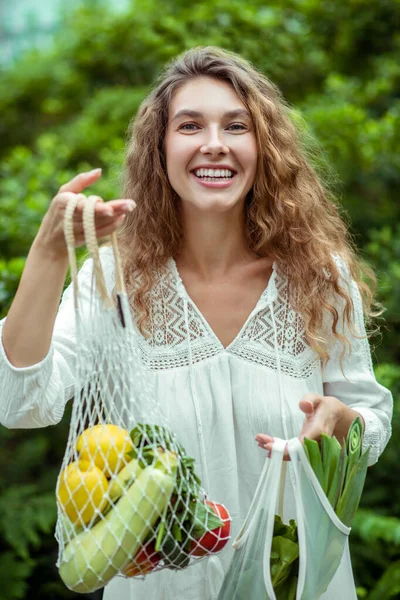 Vrouw in witte jurk holding tassen met verschillende groenten — Stockfoto