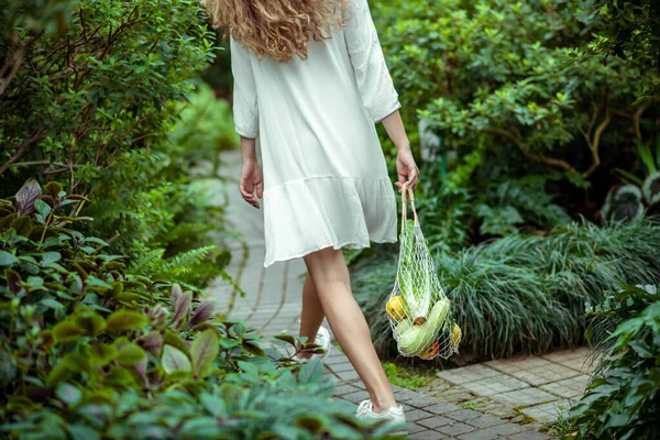 Vrouw in witte jurk walsen en het dragen van tassen met verschillende groenten — Stockfoto