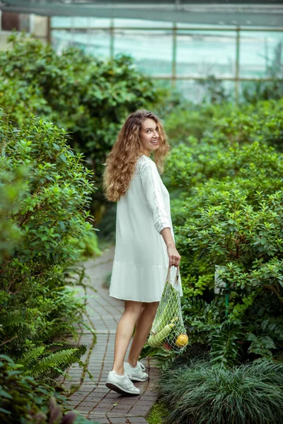 Vrouw in witte jurk draagtassen met verschillende groenten en een goed gevoel — Stockfoto