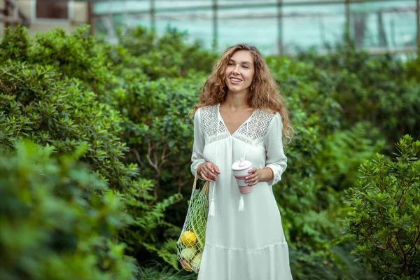 Frau im weißen Kleid mit Gemüsebeuteln in einem Gewächshaus — Stockfoto