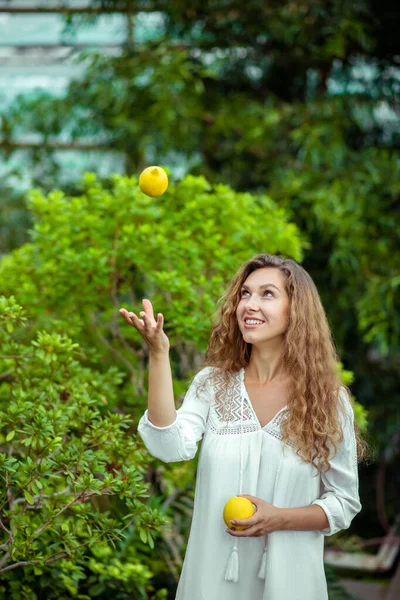 白いドレスを着た女が木の近くに立ってレモンを投げ — ストック写真