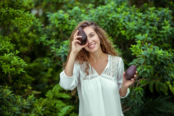 Beyaz elbiseli kadın elinde avokado, bir gözünü kapatıyor. — Stok fotoğraf