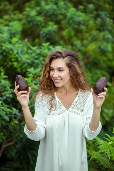 Woman in white dress standing with avocado in hands and smiling — Stock Photo, Image