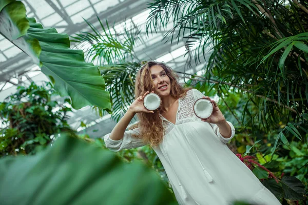 Mujer vestida de blanco con coco en las manos en invernadero — Foto de Stock