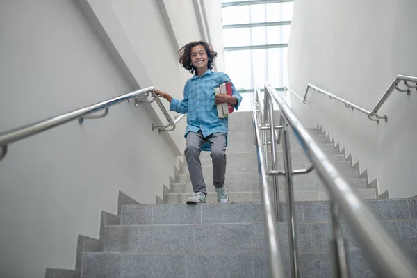 Excited schoolboy holding pile of books, running downstairs