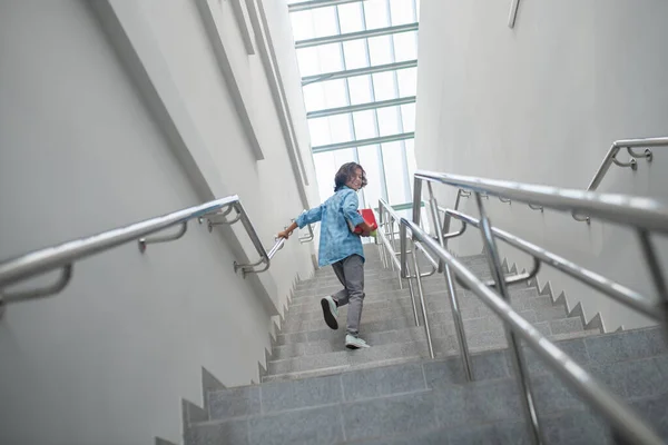 Smiling schoolboy walking upstairs with pile of books