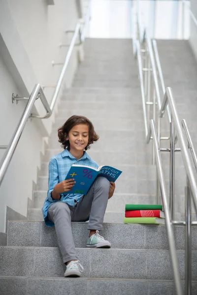 Çocuk elinde kitapla şehrin merdivenlerinde oturuyor. — Stok fotoğraf