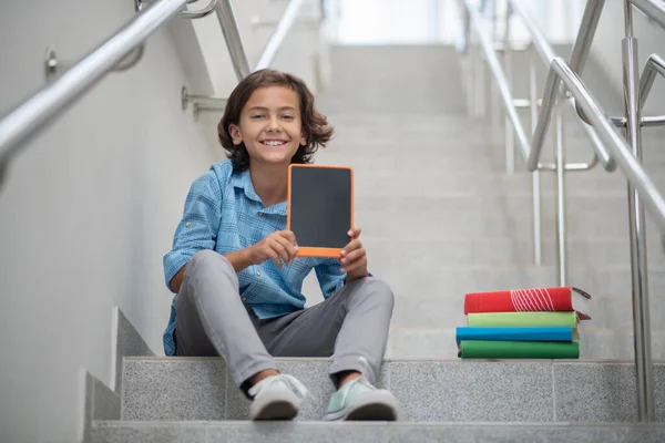 Escolar sonriente sentado en las escaleras, mostrando la tableta a la cámara — Foto de Stock