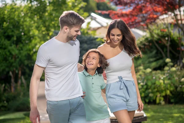 Familj om tre omfamnar varandra, går på gräsmatta — Stockfoto