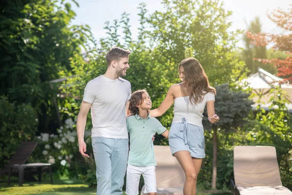 Familj på tre personer som omfamnar varandra, vandrar i semesterparken — Stockfoto