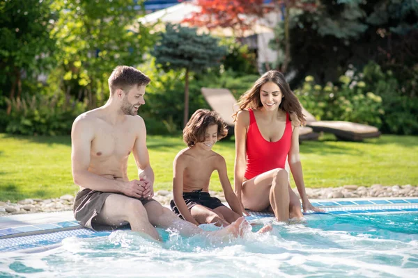 Niño con los padres sentados en el borde de la piscina — Foto de Stock