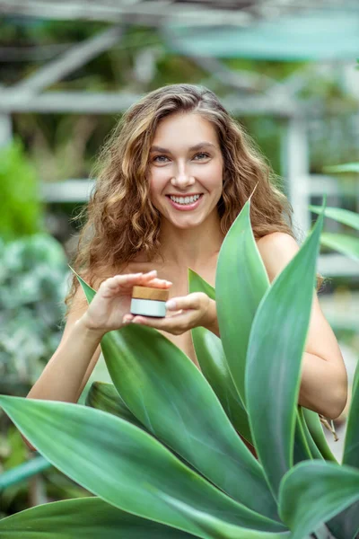 Donna vicino alla pianta con un barattolo di crema per il viso — Foto Stock