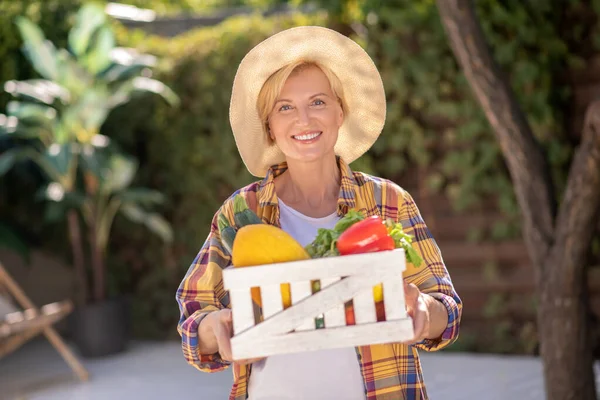 Glimlachende blonde vrouw in stro hoed holding mand met groenten — Stockfoto