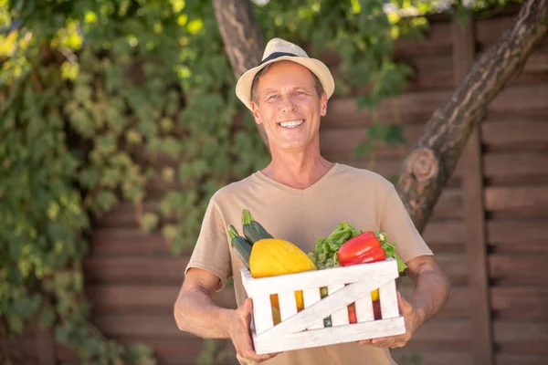 Maschio sorridente in cappello di paglia cesto con verdure — Foto Stock