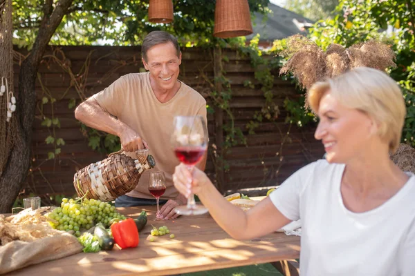 Homme versant du vin dans un verre, femme blonde tenant un verre de vin rouge, souriant — Photo