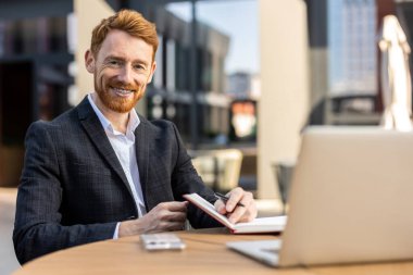 Şehir kafesinde kağıt defter kullanan profesyonel takım elbiseli bir genç.