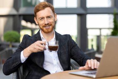 Kafkasyalı profesyonel elinde kahveyle laptopta e-postaları kontrol ediyor.